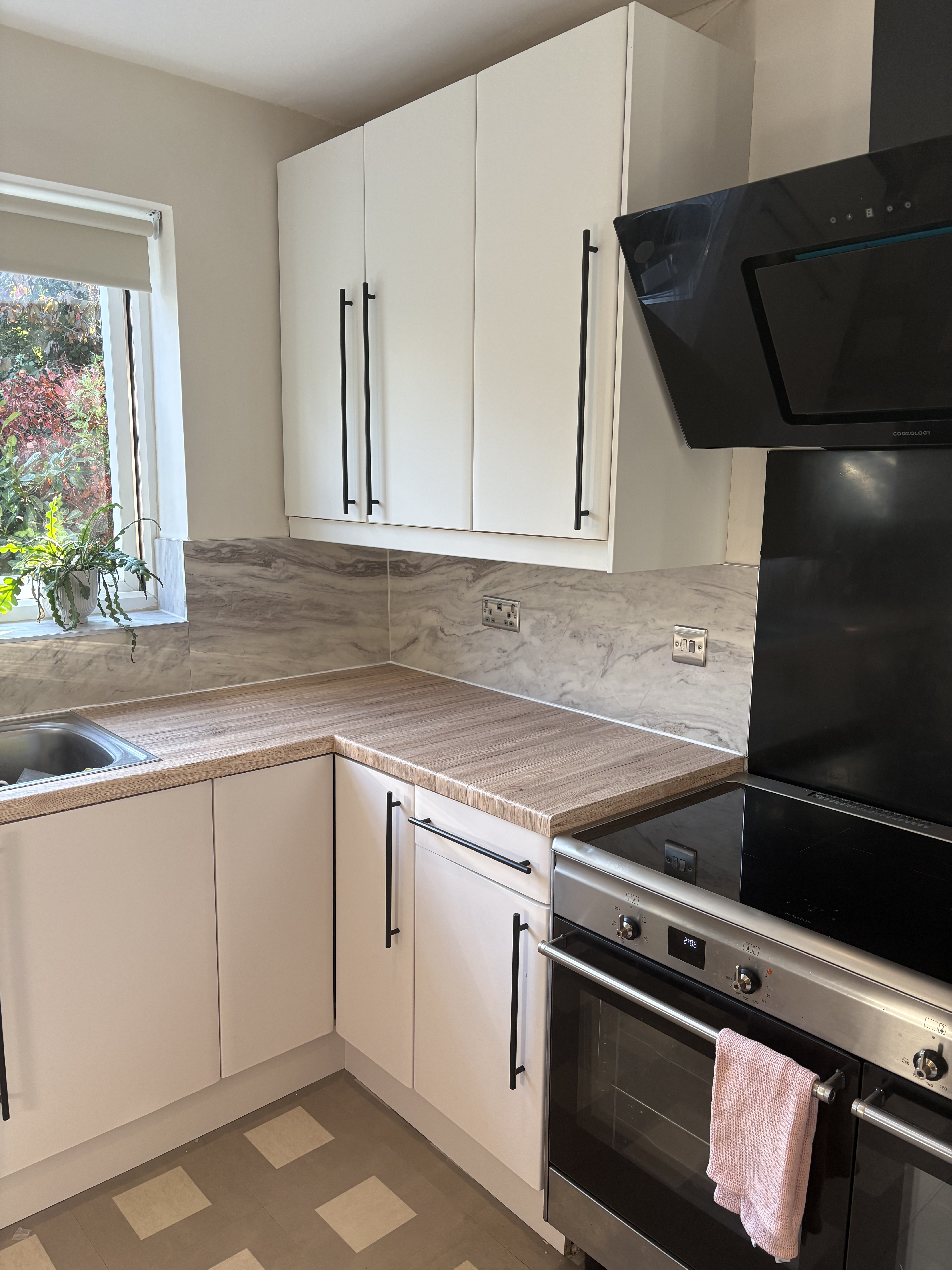 A professionally wrapped kitchen with white cabinetry, a wood-grain worktop, a black range cooker and a marble-effect backsplash